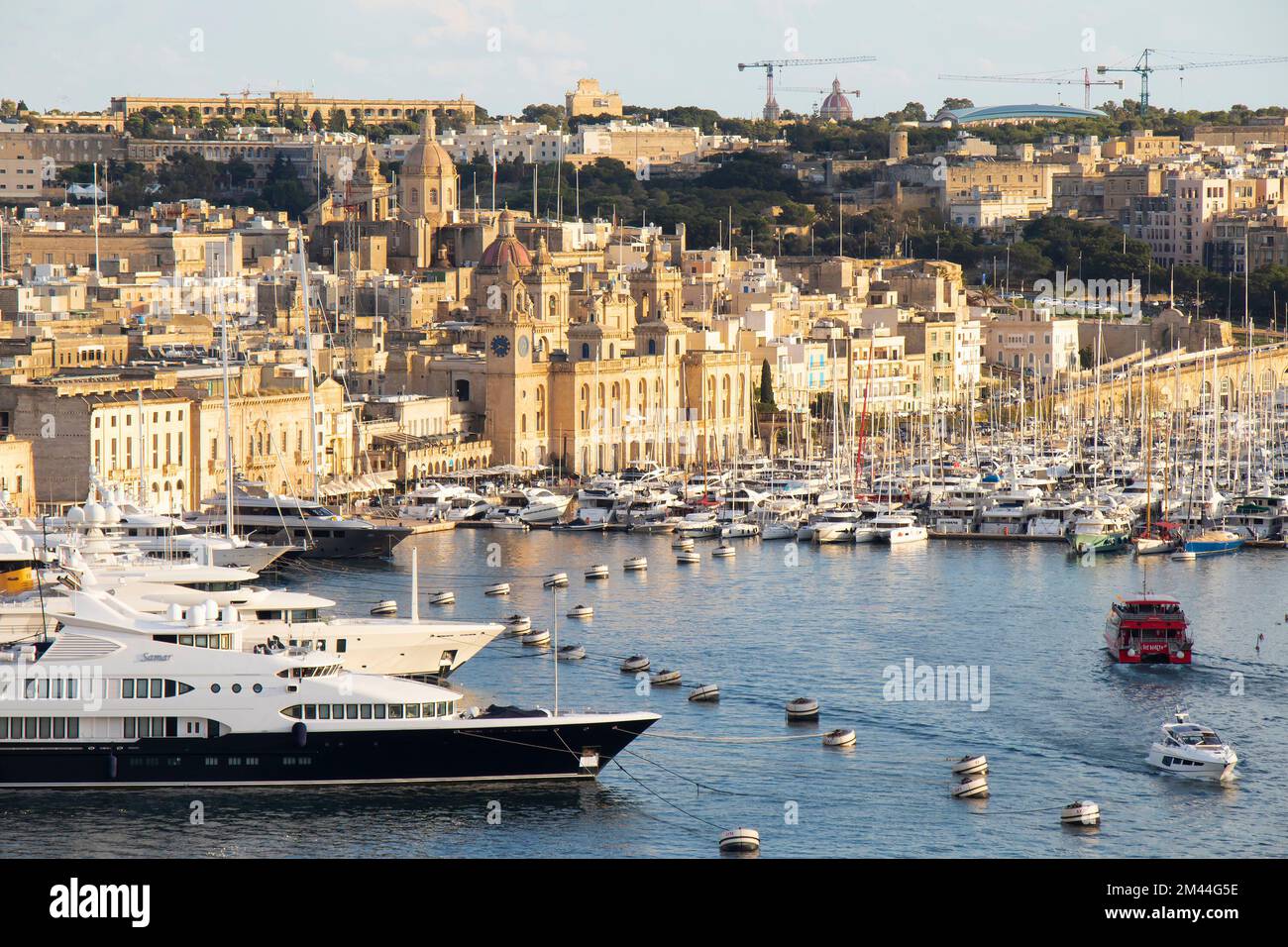Birgu, Malta - November 13, 2022: Cityscape with stone facades shining in sunset and grand harbour marina with moored yachts and sailing ships Stock Photo