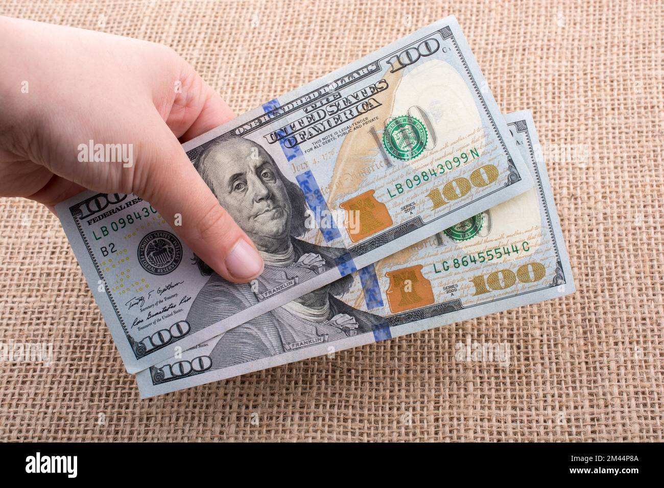 Hand holding banknote bundle of US dollar on a linen canvas background ...