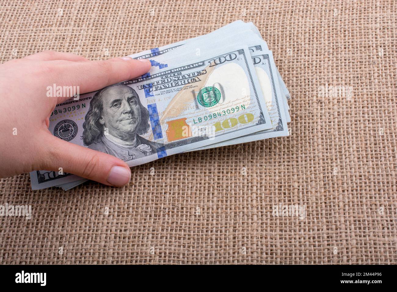 Hand holding banknote bundle of US dollar on a linen canvas background ...