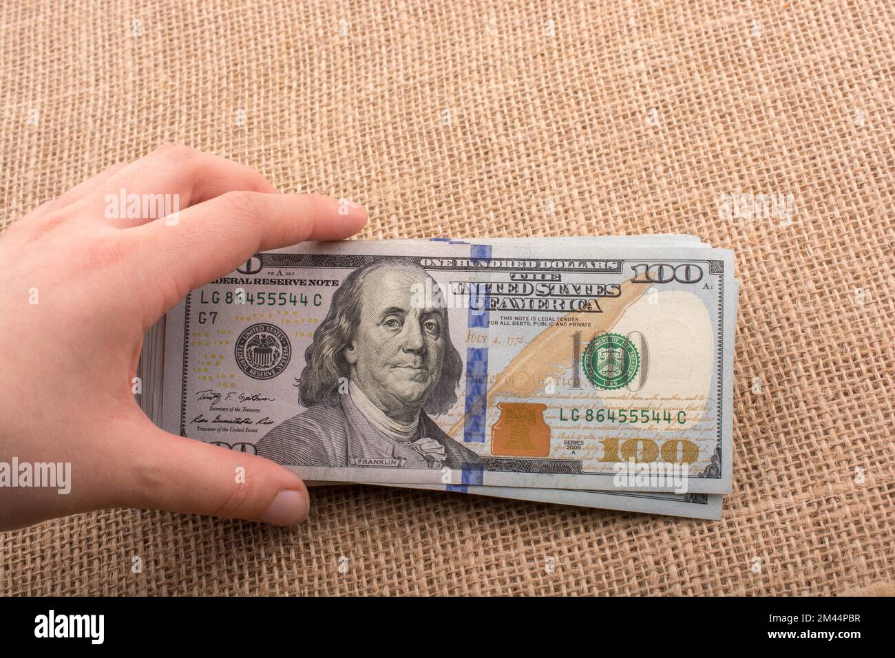 Hand holding banknote bundle of US dollar on a linen canvas background ...