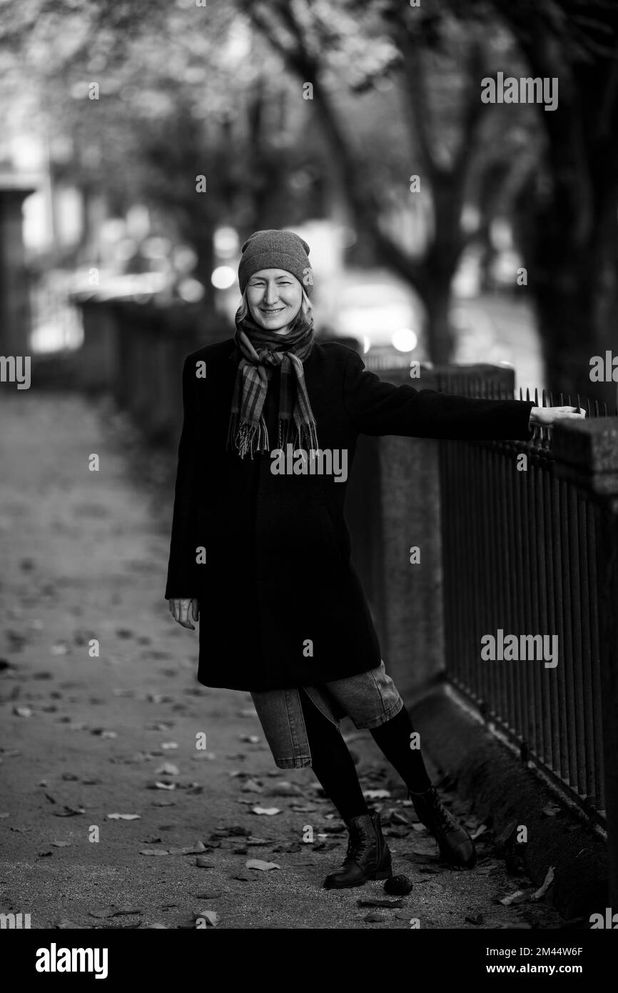 Woman in a coat posing near a park fence. Black and white photo. Stock Photo