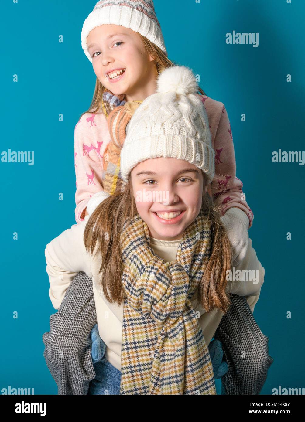 Two sisters or teenage friends play leapfrog. Winter motif and clothes. studio photo. Sweaters, scarves, gloves. Joy on the faces. vertically on a blu Stock Photo