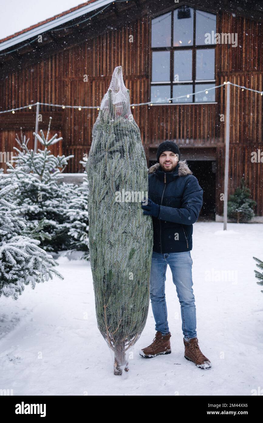 Young man stand by Christmas tree. Big tree for big family. Happy winter holidays Stock Photo