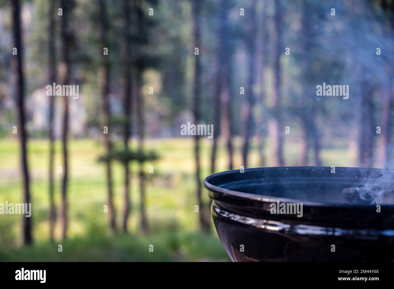 Focus on a portable charcoal grill at a campsite overlooking a green