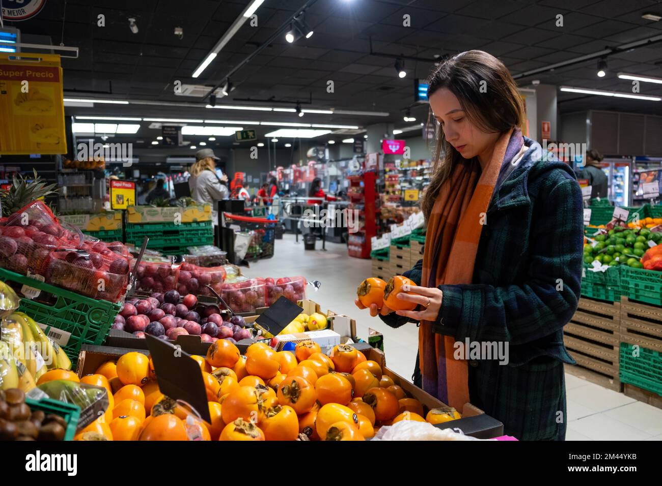 Young latin woman choosing fruits in a grocery store. Persimmon fruit Stock Photo