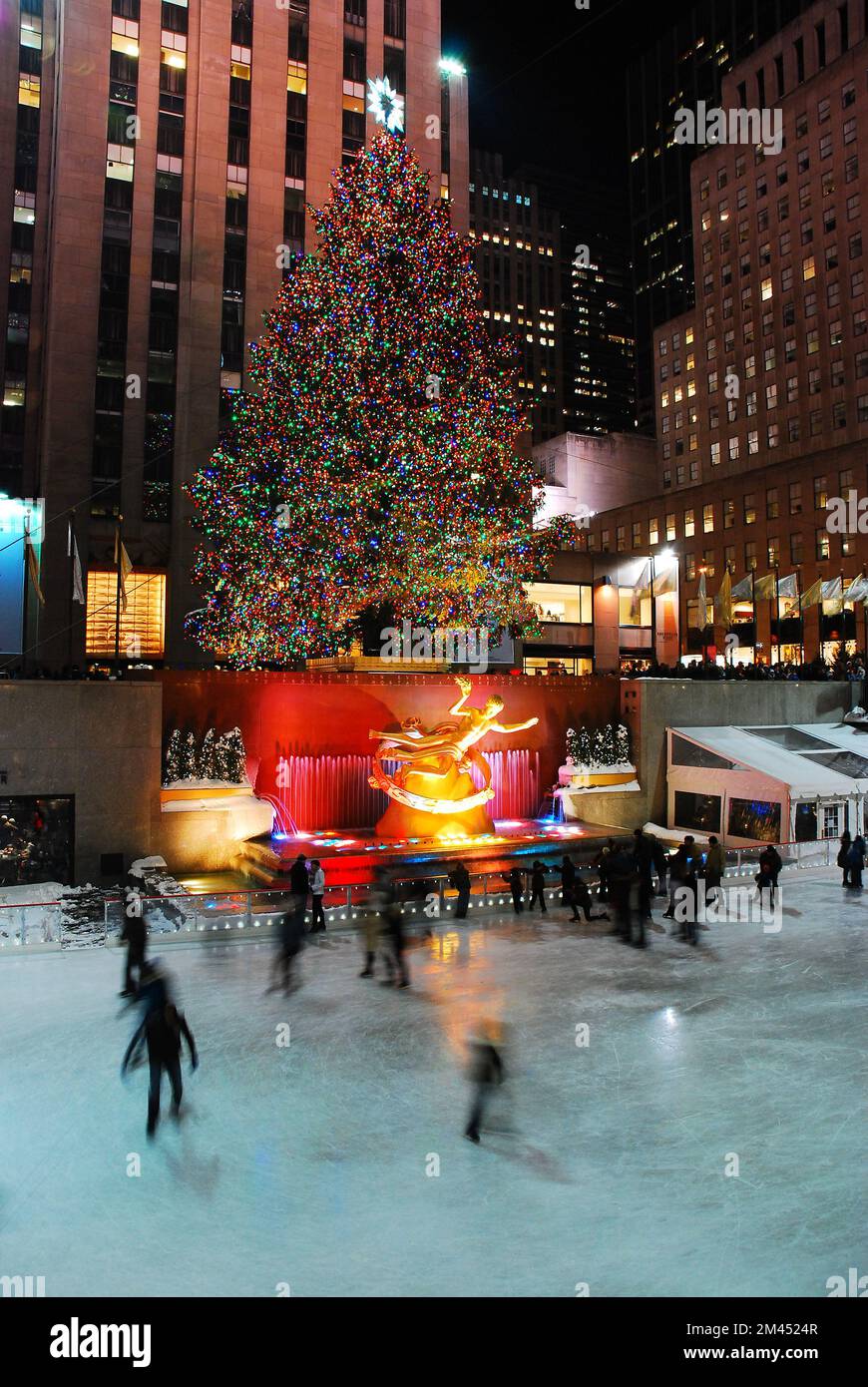 Ice Skaters glide underneath the famous Christmas tree in Rockefeller Center, New York City, in winter Stock Photo