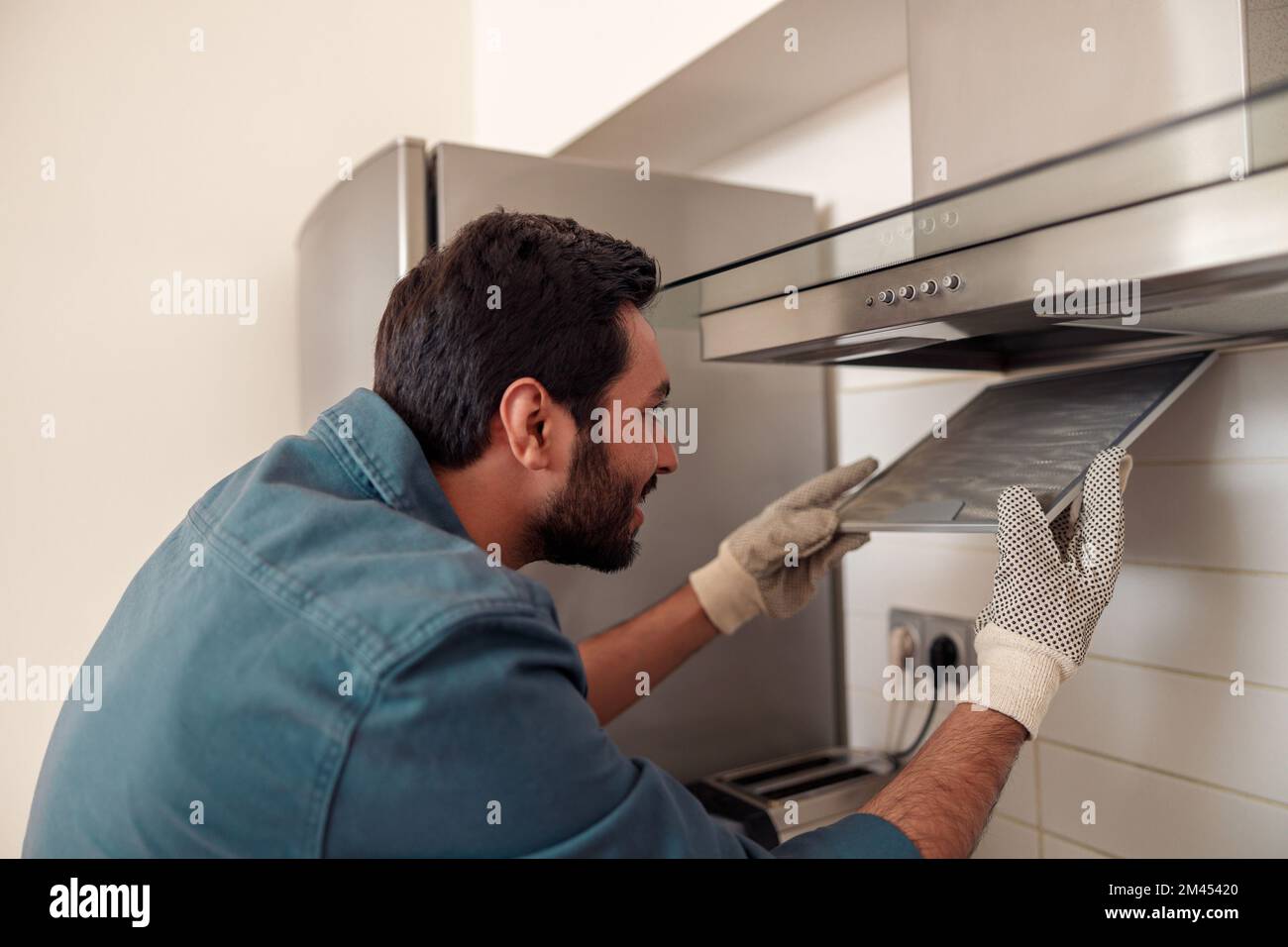 Handyman in uniform repairing kitchen extractor, replacing filter in