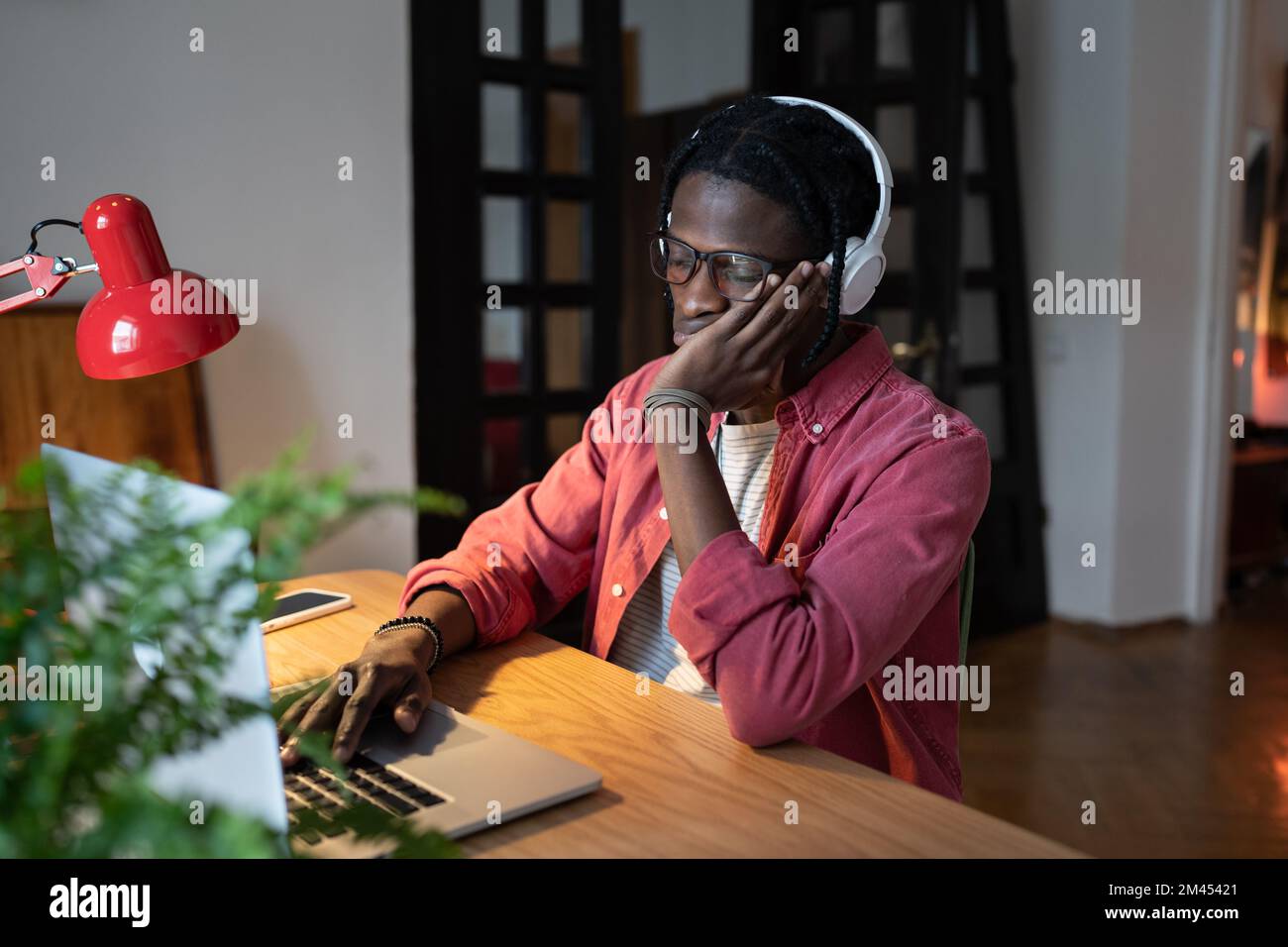 Tired African student guy feeling sleepy while studying online on laptop for long hours at home Stock Photo