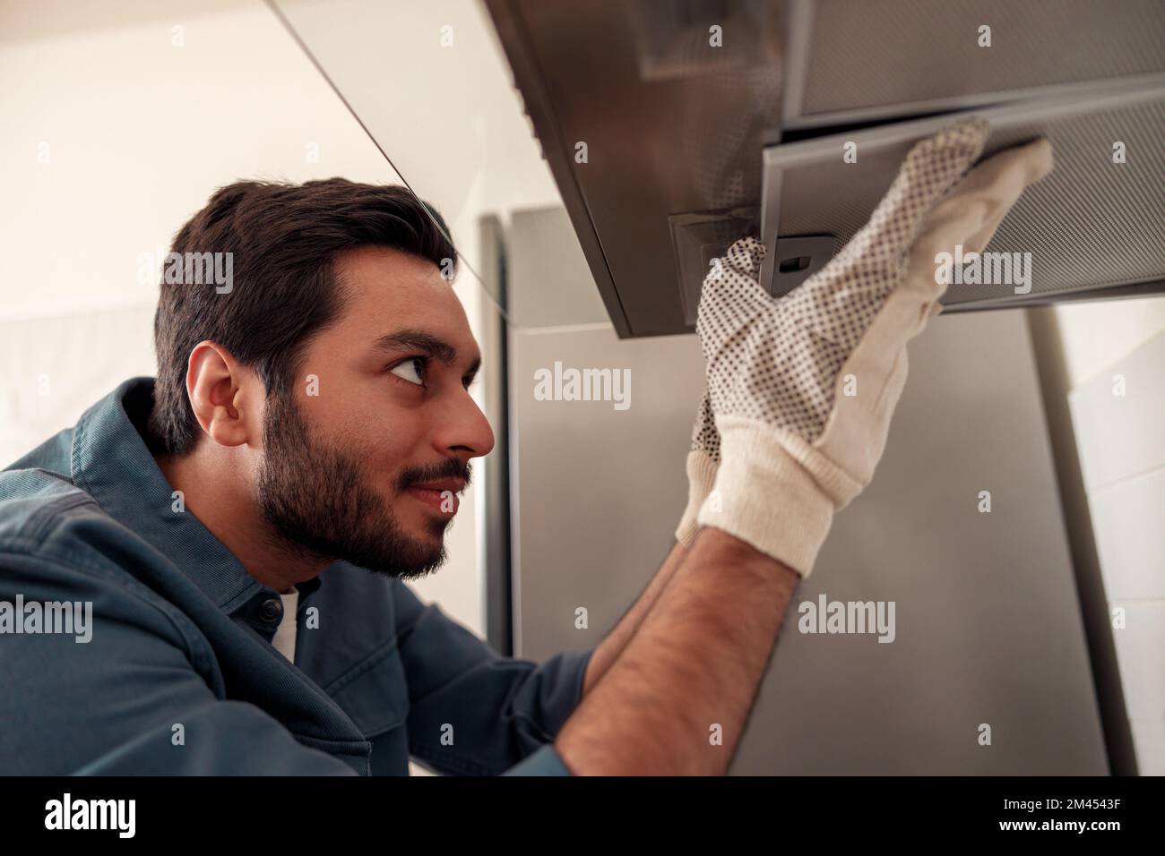 Handyman in uniform repairing kitchen extractor, replacing filter in