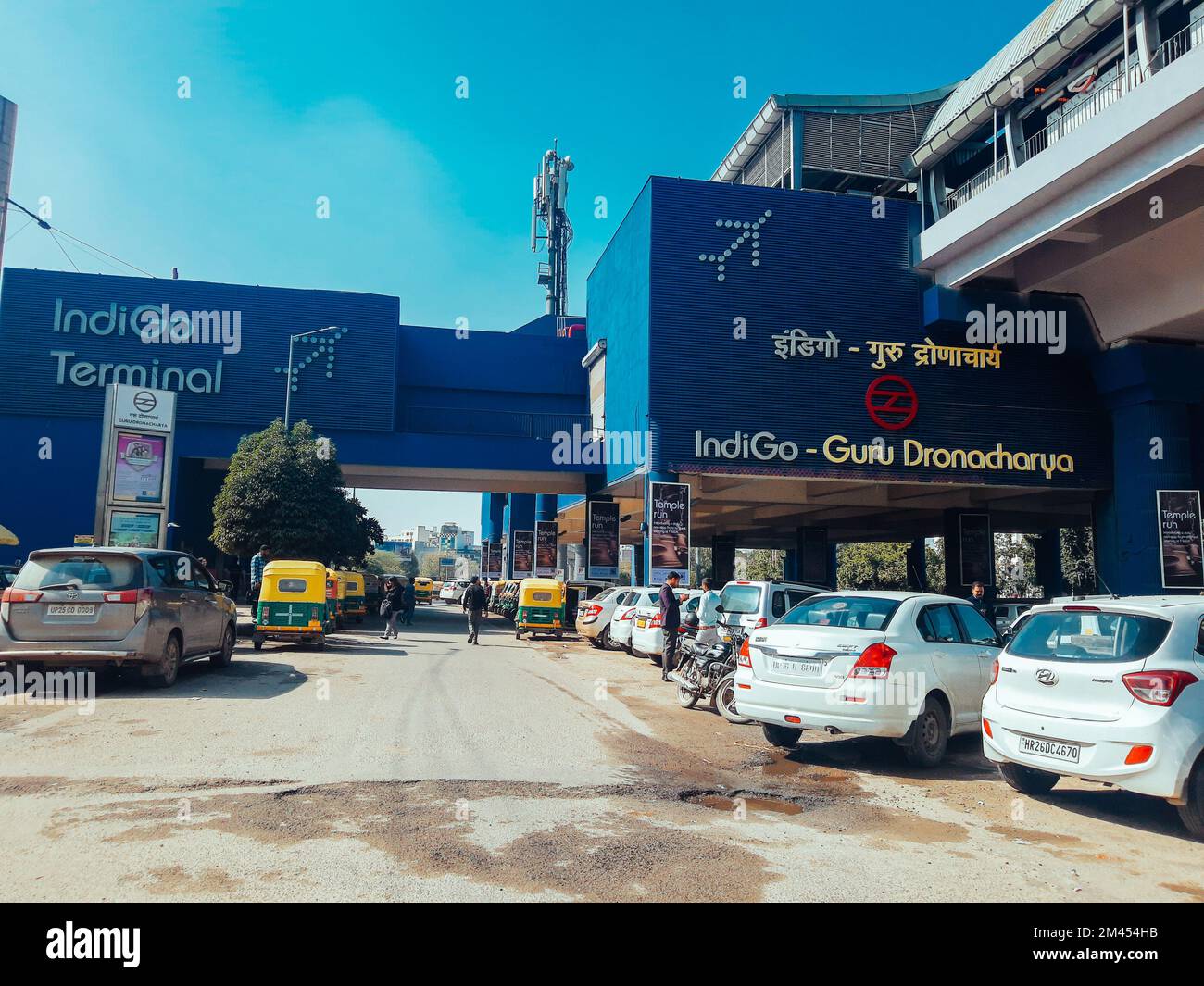 A street view of parked cars, walking people by Guru Dronacharya metro