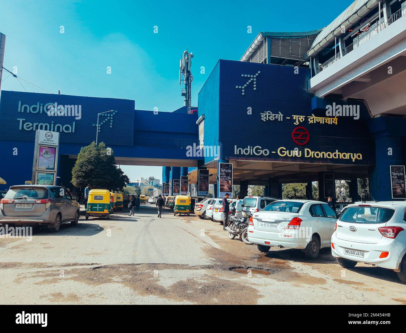 A street view of parked cars, walking people by Guru Dronacharya metro station near Global Business Park in Delhi, India Stock Photo