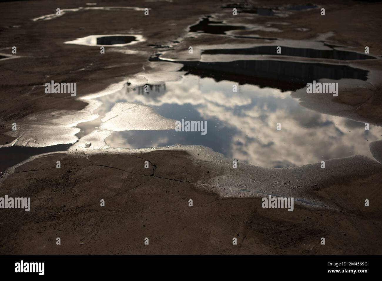 Large puddle on asphalt. Puddle after rain. Precipitation in city. Reflection of clouds in water. Stock Photo