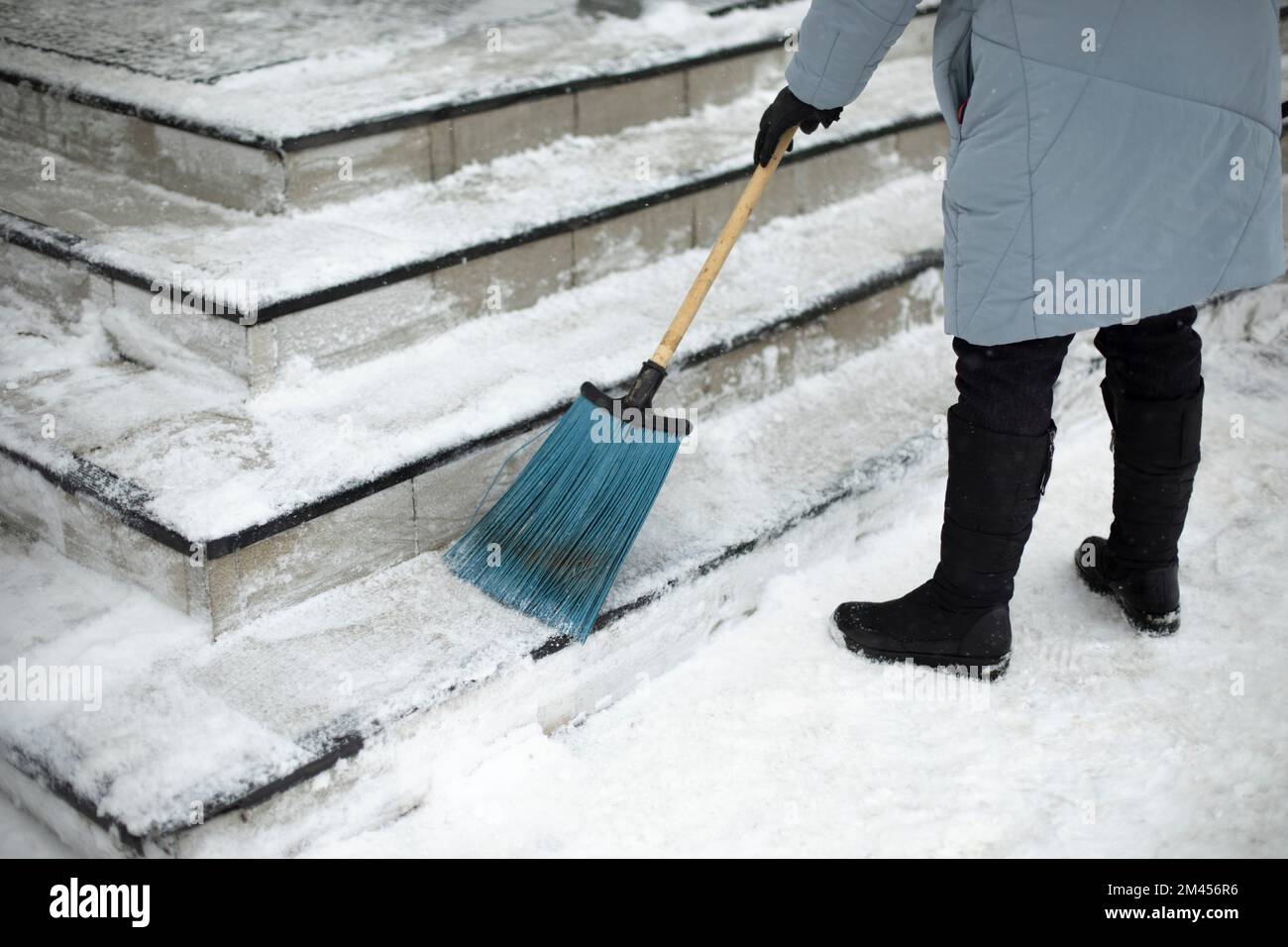 Snow removal from steps. Woman sweeps snow from street with broom