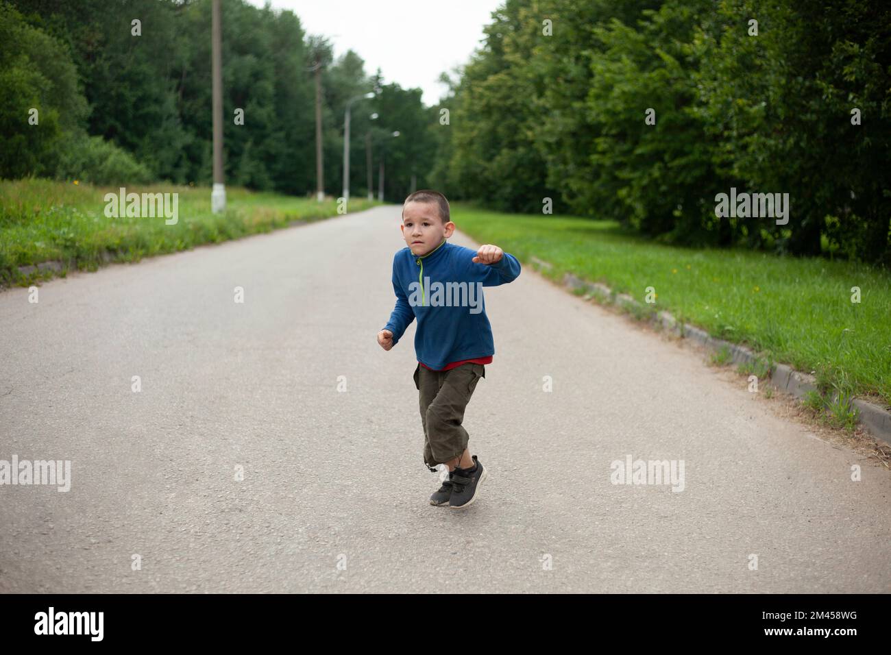 Child runs down road. Boy in summer. Schoolboy on street. Street boy in town. Stock Photo