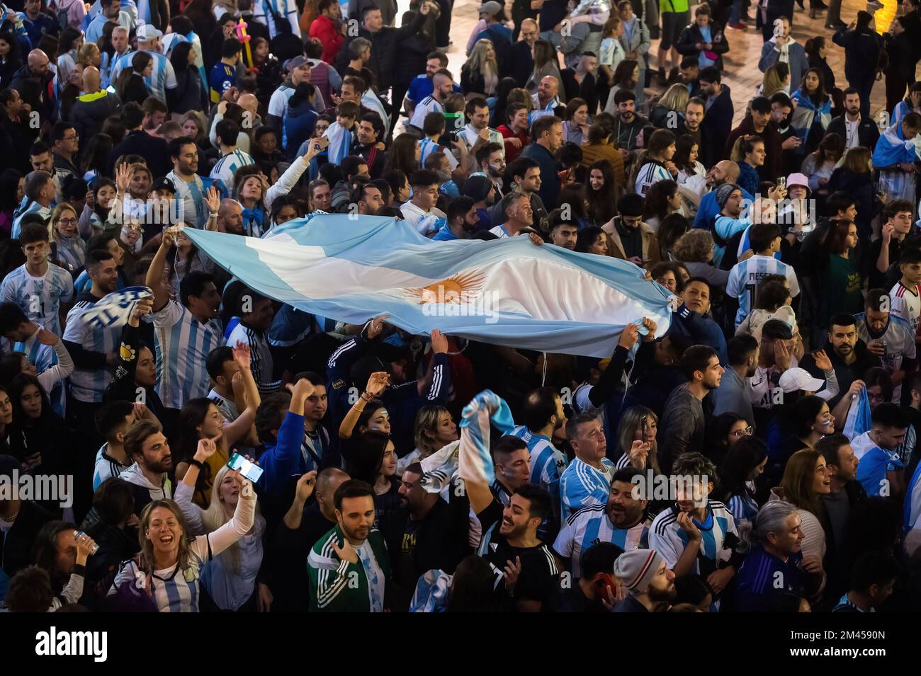 Malaga, Spain. 18th Dec, 2022. Argentinian fans are seen holding a large flag as they celebrate the Argentina's victory at Plaza de la Constitucion square. Under a festive atmosphere, thousands of Argentinian residents in the city of Malaga have taken to the streets of the city center to celebrate the victory of the Argentine national football team, following their victory against France during the final of the FIFA World Cup Qatar 2022. Credit: SOPA Images Limited/Alamy Live News Stock Photo