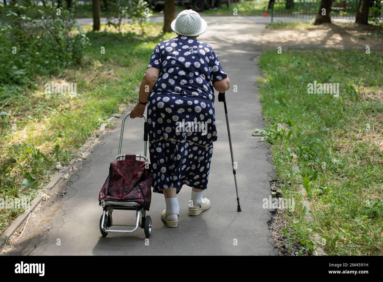 Old woman with walking stick. Pensioner in Russia. Woman with bag walks