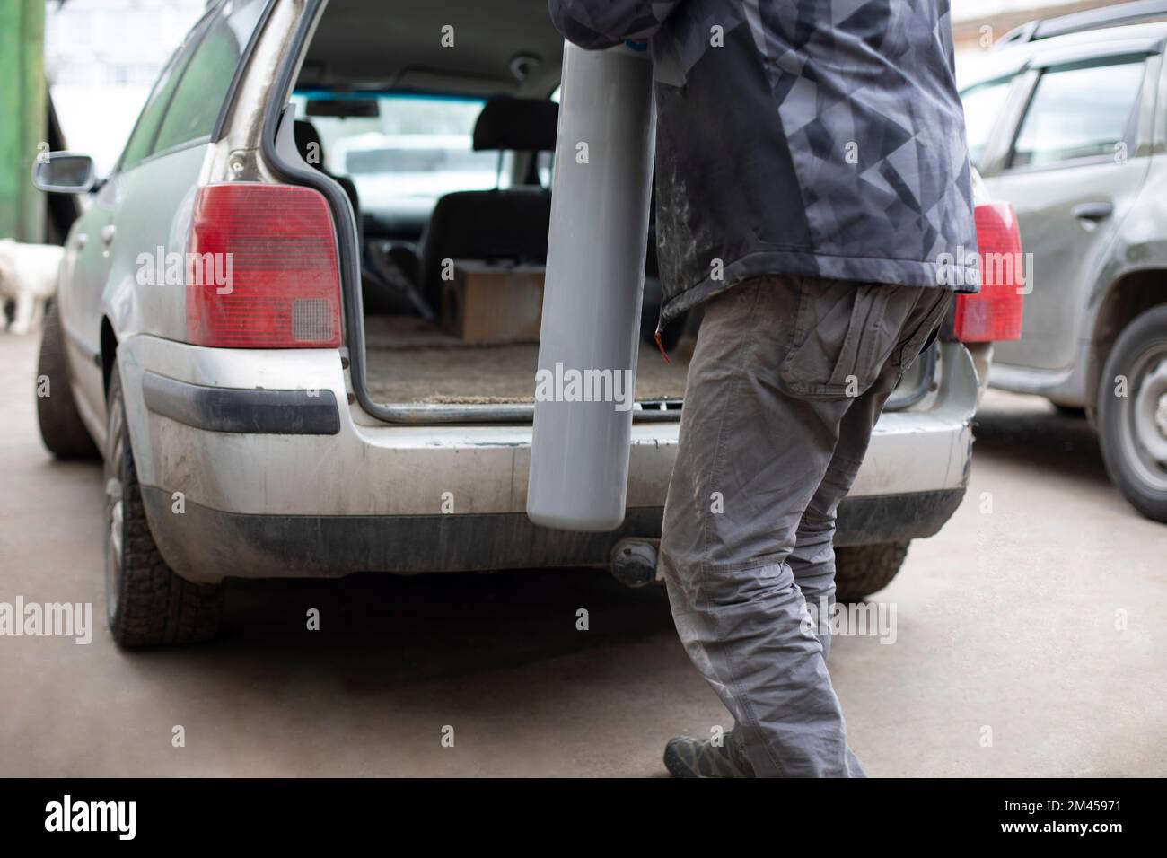 Man puts gas cylinder in trunk of car. Dangerous cargo in transport. Worker transports liquefied