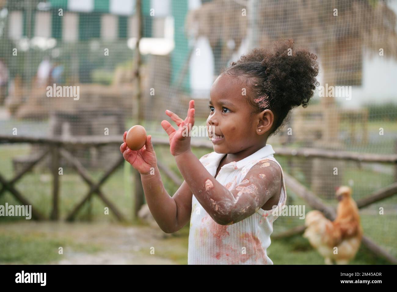 African-American child holding chicken egg with color stain on hand and dress. Stock Photo