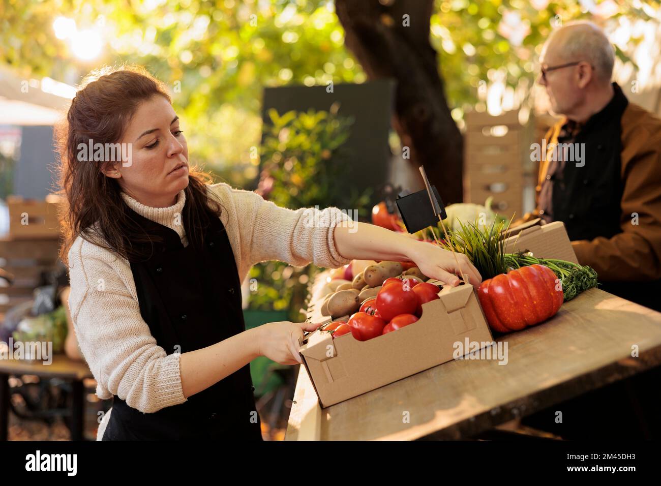 Female farmers market vendor arranging fresh organic produce stall in