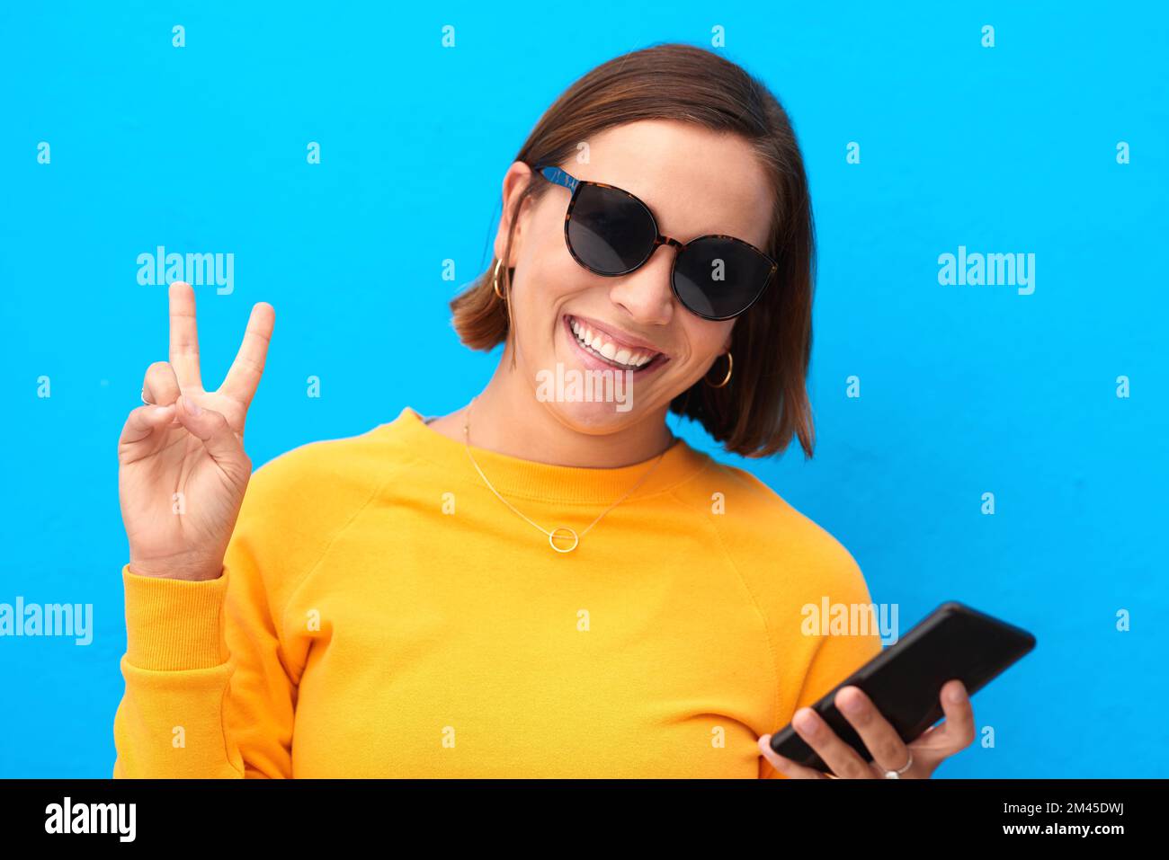 Peace out folks. Cropped portrait of a happy young woman showing the peace sign against a blue background. Stock Photo