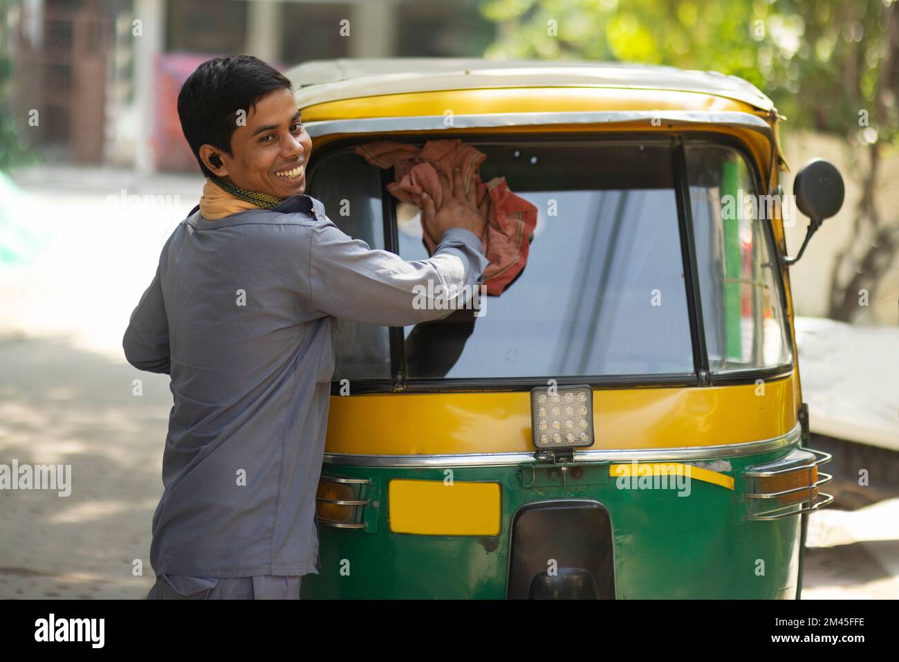 Young man cleaning front glass of his auto rickshaw Stock Photo