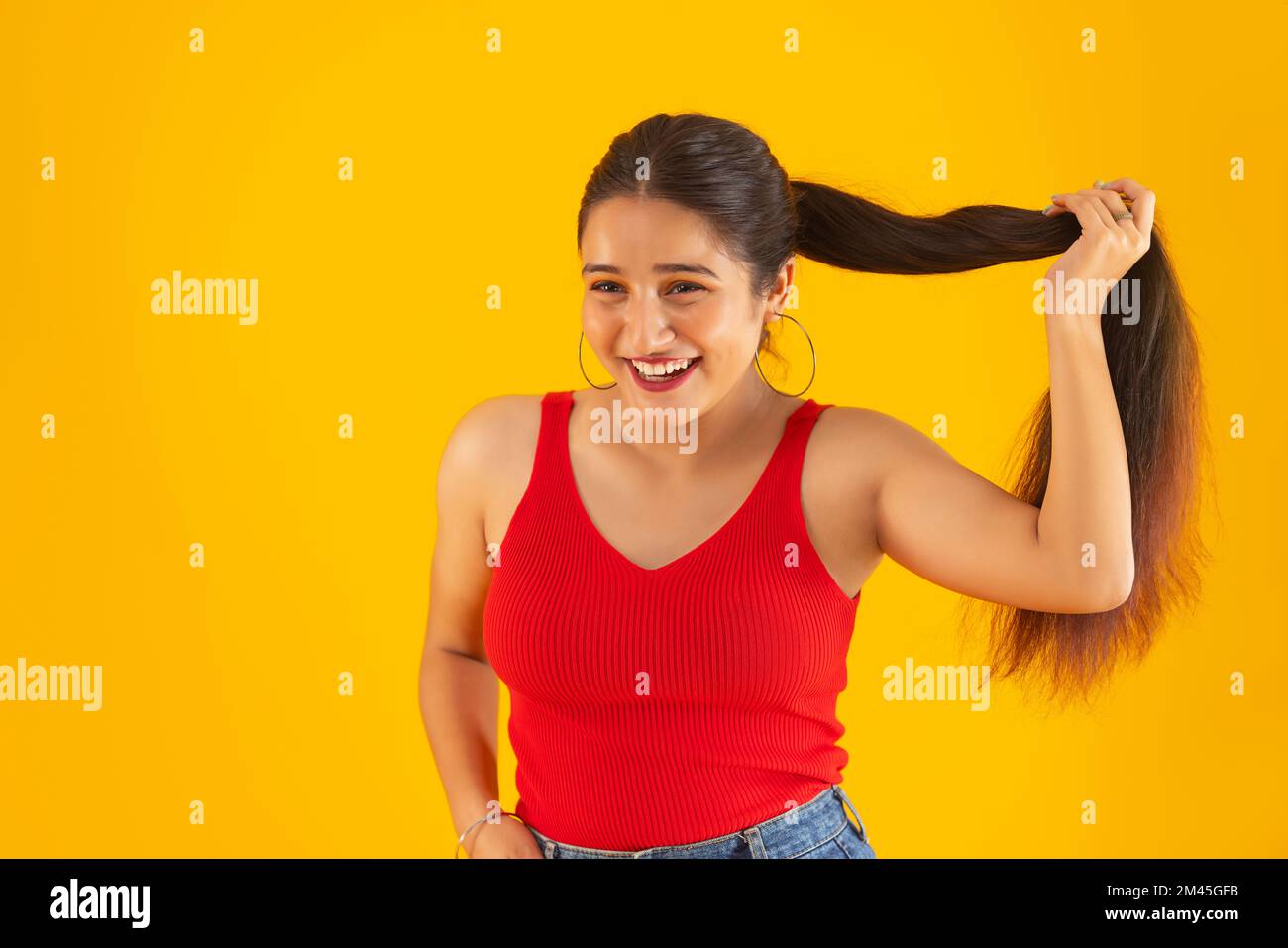 Smiling teenage girl holding her hair against yellow background Stock Photo