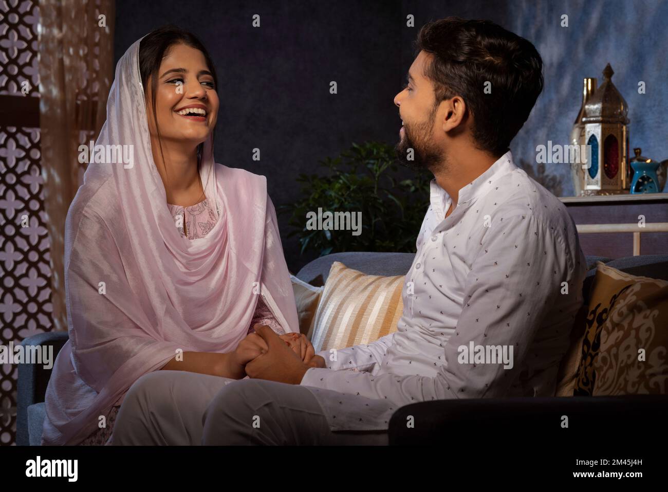 Romantic Muslim couple holding hands and looking at each other in living room Stock Photo