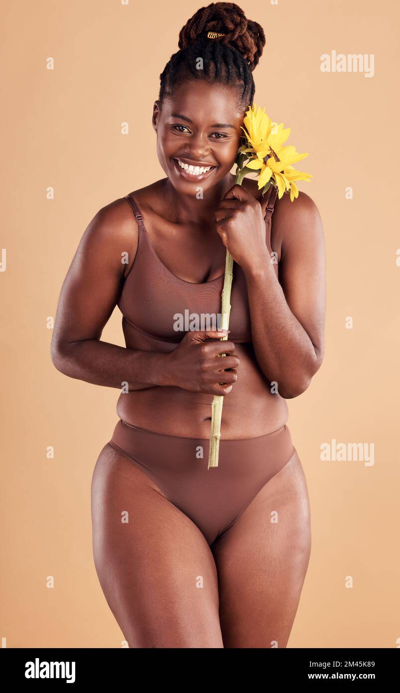 Beauty, wellness and portrait of black woman with sunflower in studio for skincare, self care and self love. Health, cosmetics and plus size girl with Stock Photo