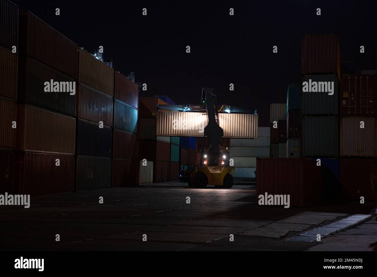 Reach Stacker during operation. Reach-stacker container loader during night work. Industrial port container terminal. Container stacker in the port at Stock Photo