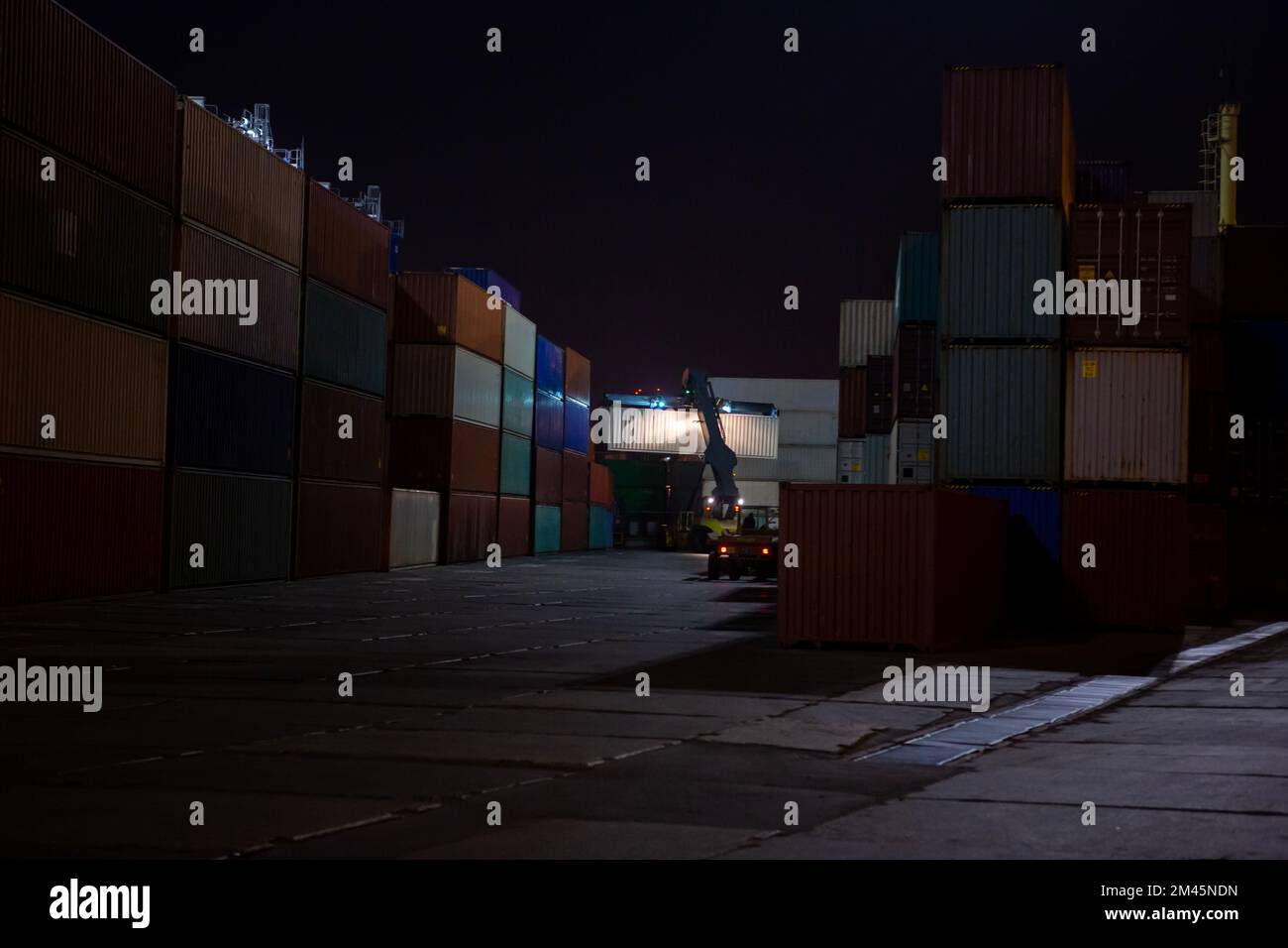 Reach Stacker during operation. Reach-stacker container loader during night work. Industrial port container terminal. Container stacker in the port at Stock Photo