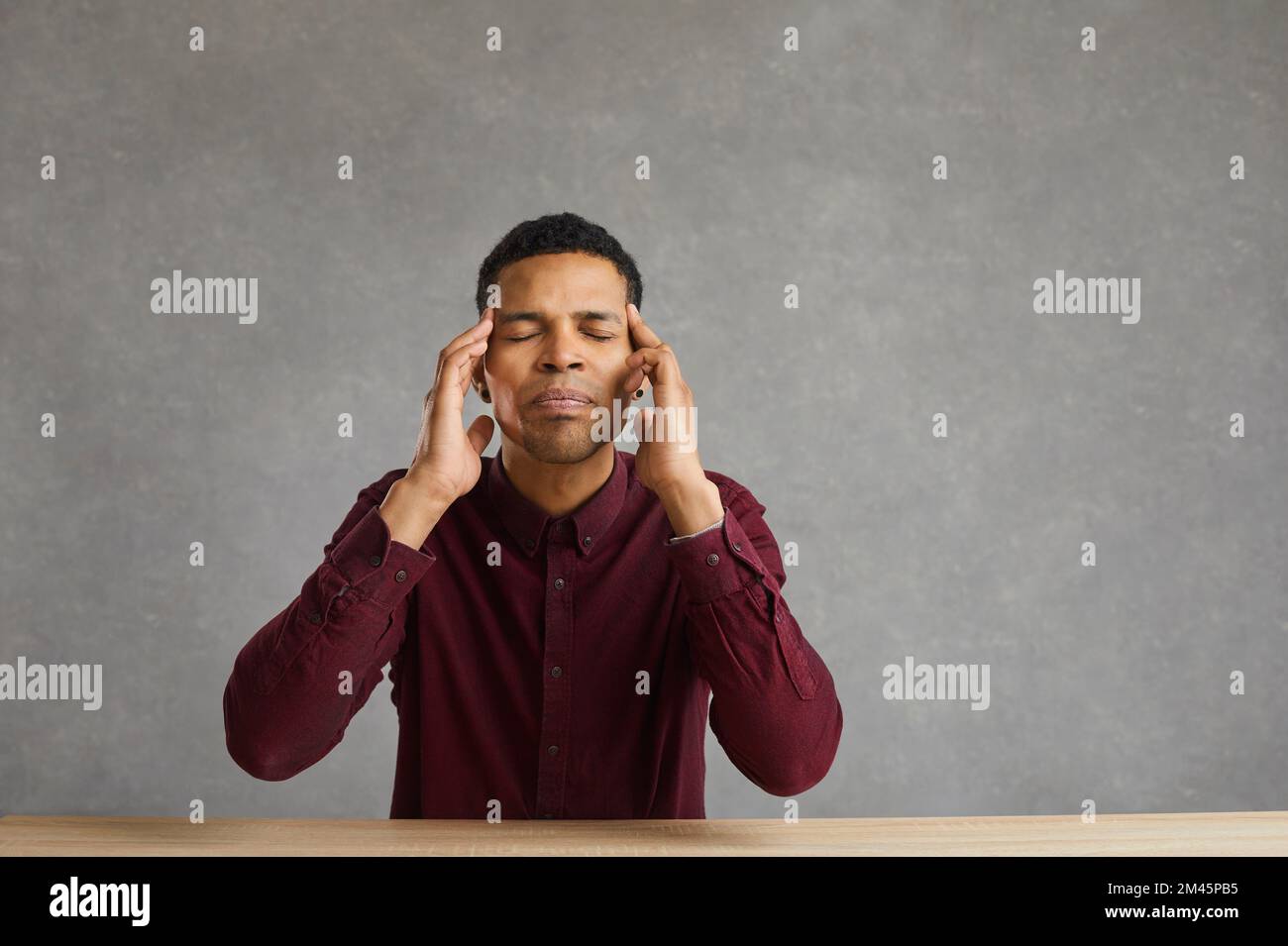 Tired black man sitting at desk and massaging temples trying to calm ...