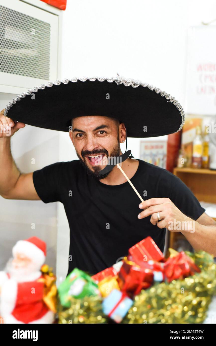 Mexican man in sombrero holding mustache on a stick and smiles in the camera Stock Photo