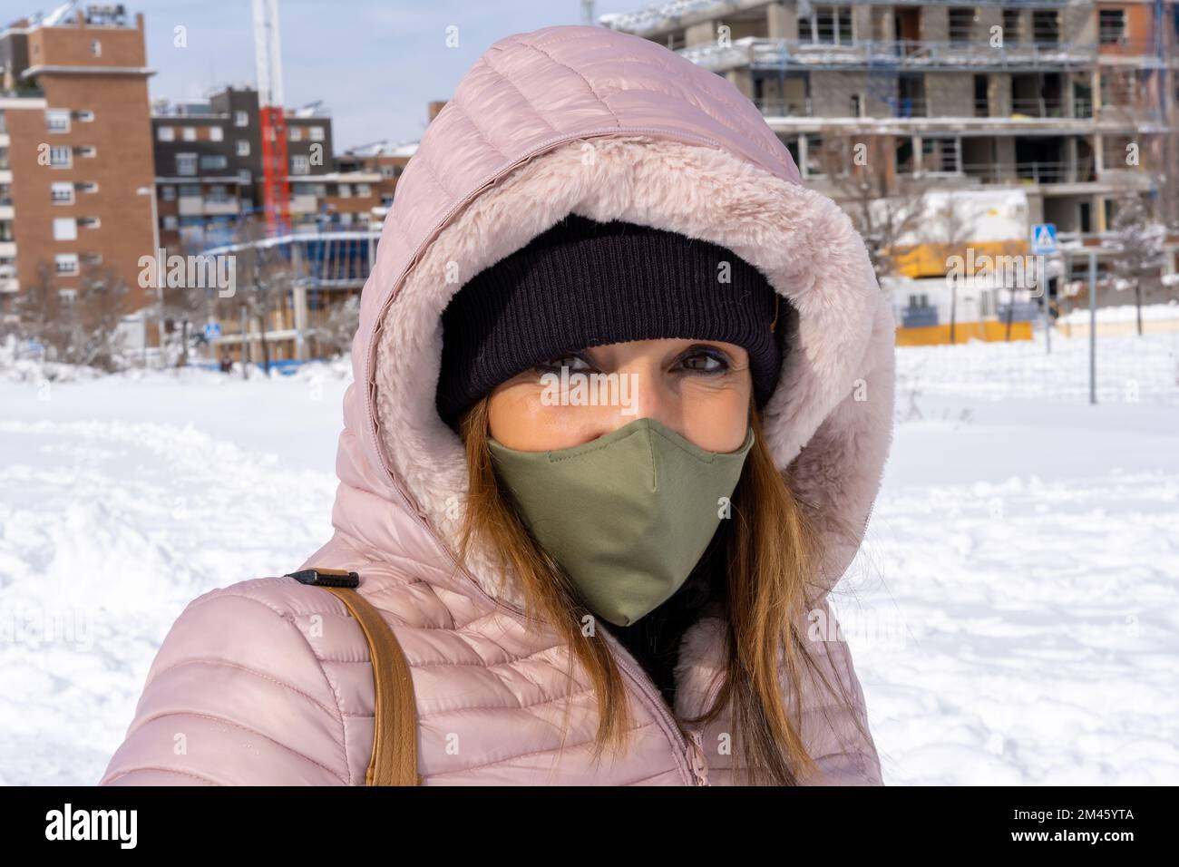Woman with a face mask looking at camera while standing outdoors in a wintry day. Winter concept. Stock Photo