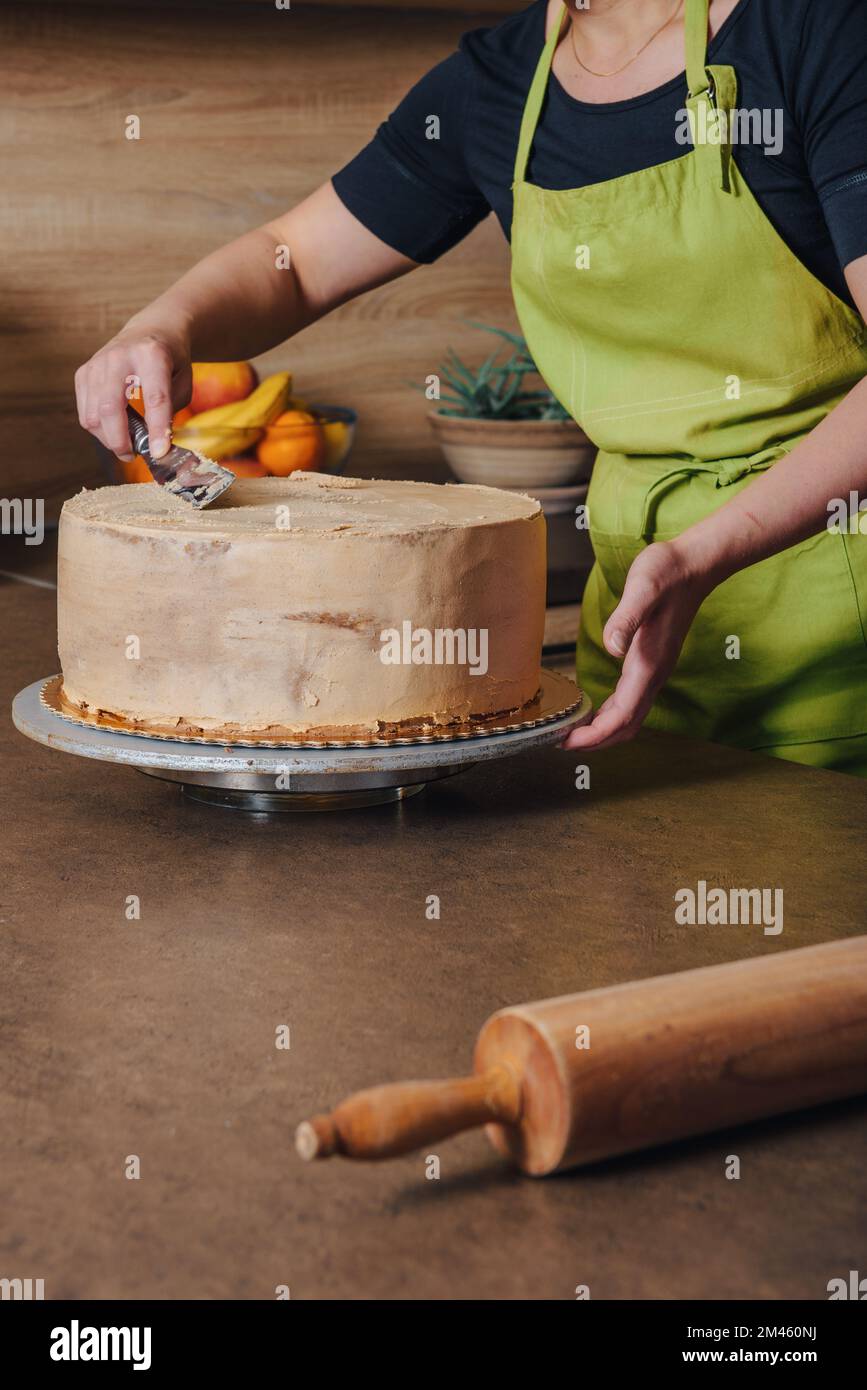 Unrecognisable woman decorating a delicious layered sponge cake with chocolate icing cream. DIY, sequence, step by step, part of series. Stock Photo