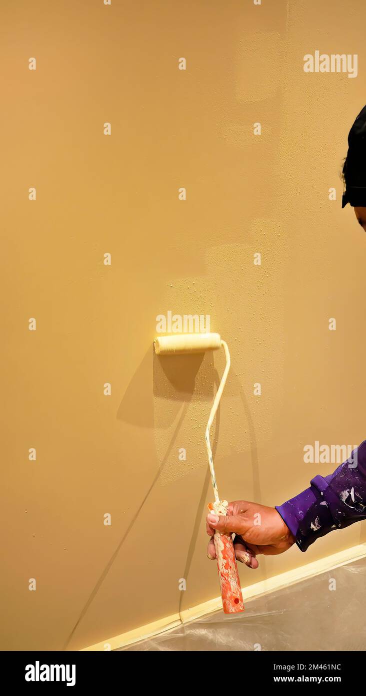 Painter man at work with paint roller painting a yellow wall, human body part, copy space, home improvement, construction Stock Photo