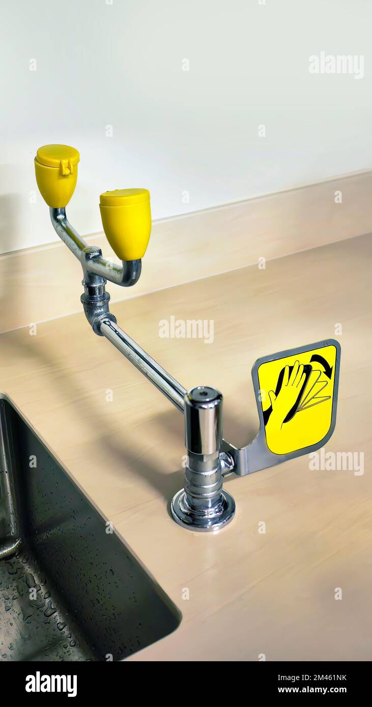 Stainless Emergency Eye Wash in yellow color installed on the counter near wash basin in the room Stock Photo