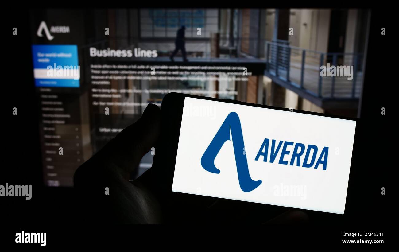 Person holding smartphone with logo of Emirati company Averda International on screen in front of website. Focus on phone display. Stock Photo