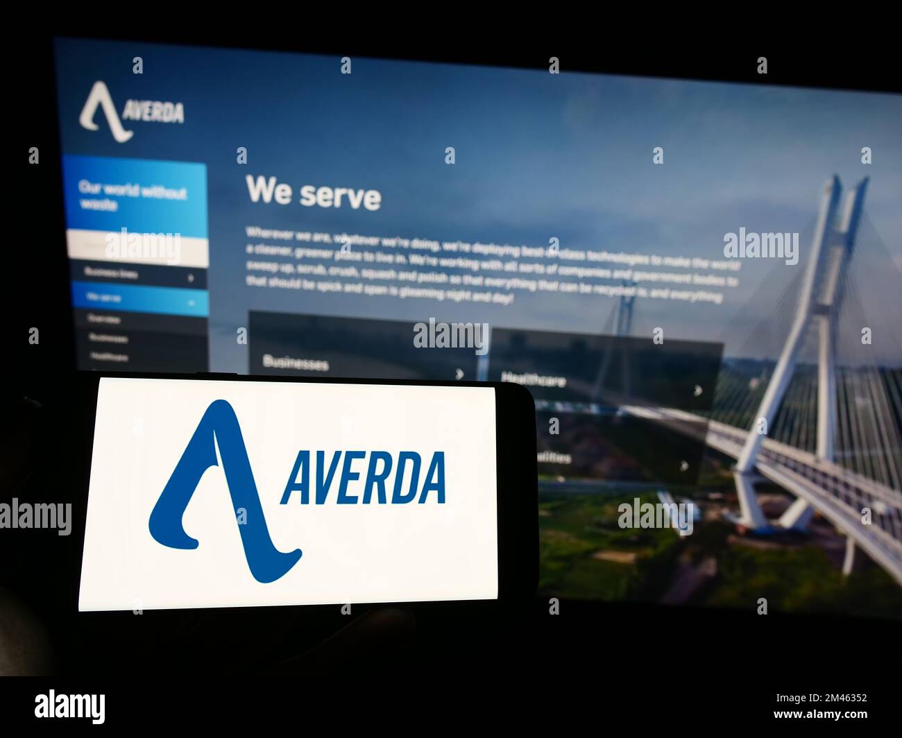 Person holding mobile phone with logo of Emirati company Averda International on screen in front of business web page. Focus on phone display. Stock Photo