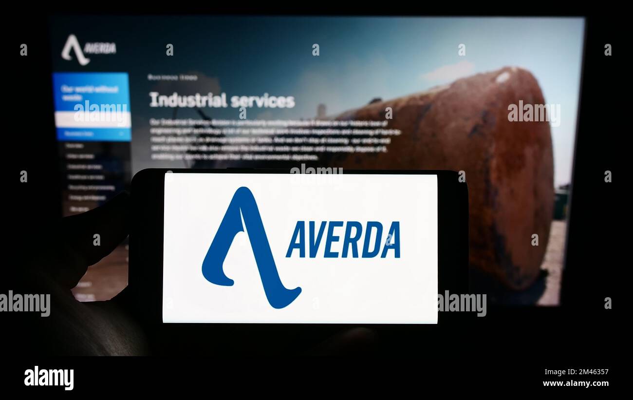 Person holding cellphone with logo of Emirati company Averda International on screen in front of business webpage. Focus on phone display. Stock Photo