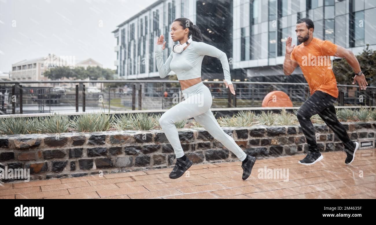 Running, fitness and couple in the rain with runner energy, speed and fast people doing sport. City, exercise and workout sports in winter doing Stock Photo