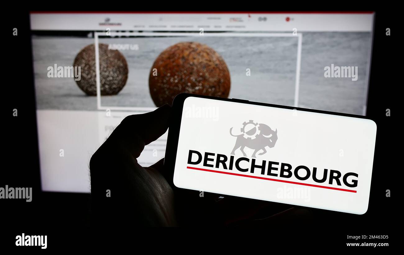 Person holding cellphone with logo of French recycling company Derichebourg S.A. on screen in front of business webpage. Focus on phone display. Stock Photo