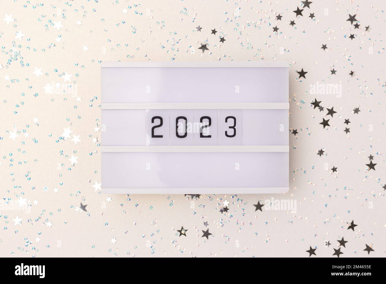 Lightbox with 2023 numbers and stars confetti scattered on a silver glittering background. New Year glowing concept. Stock Photo