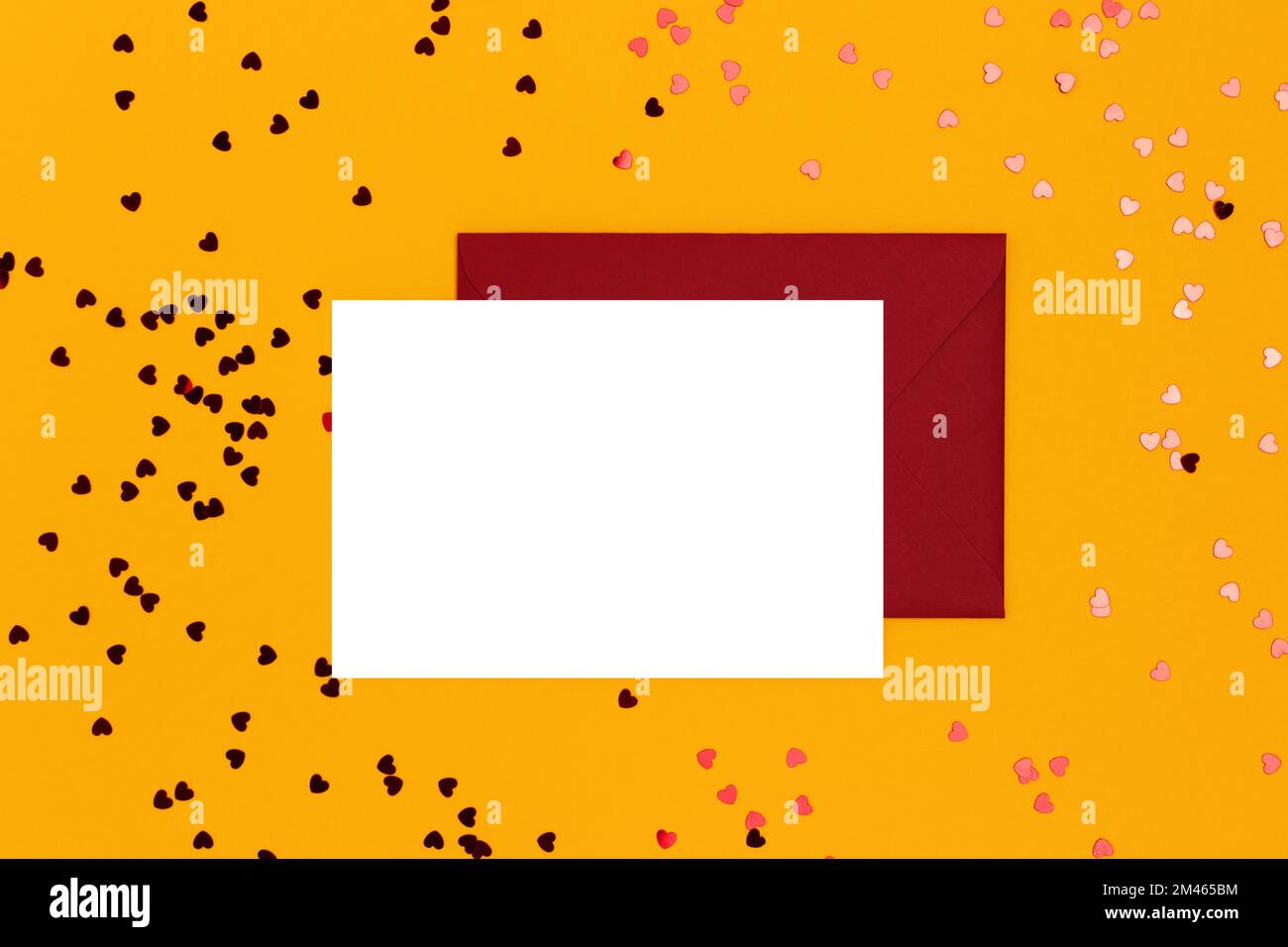 Empty white paper mockup, envelope and red hearts confetti on a yellow background. Creative concept. Stock Photo