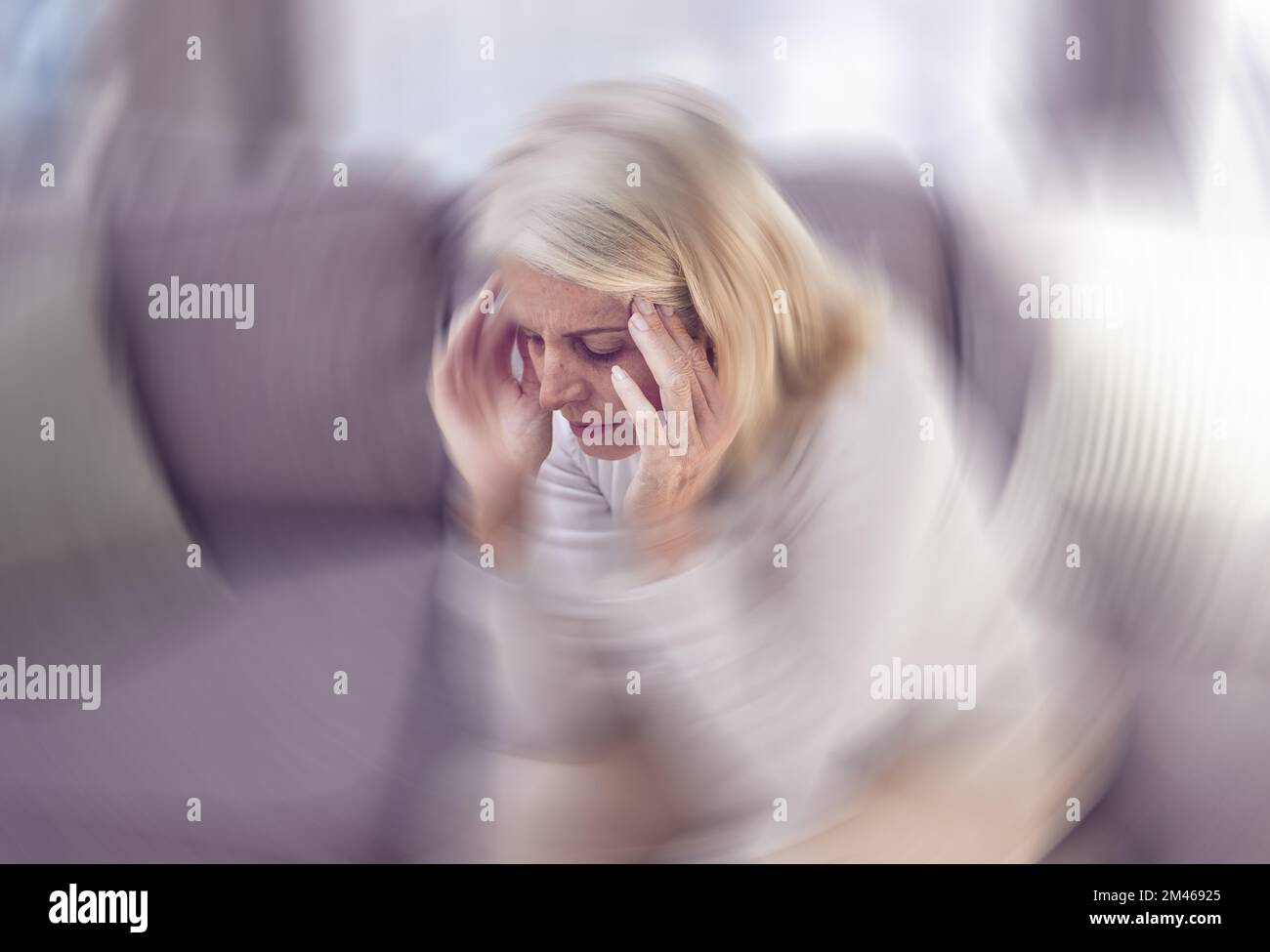 Senior woman, headache and sofa in home with motion blur, pain and depressed while tired in retirement. Elderly, old woman and anxiety with burnout Stock Photo