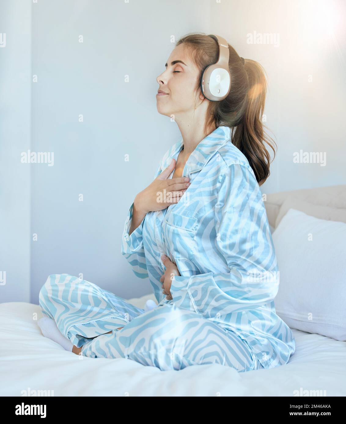 Woman, morning and headphones for meditation on bed while listening to music or podcast while breathing for chakra exercise in bedroom. Female at home Stock Photo