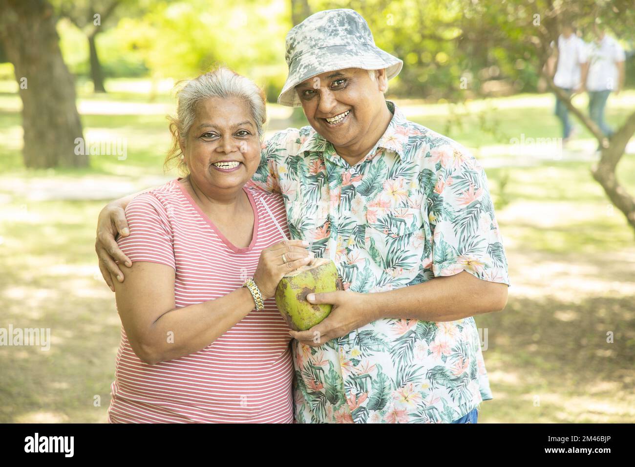 Happy indian senior couple having coconut water at summer park. Old people enjoying retirement life. Stock Photo