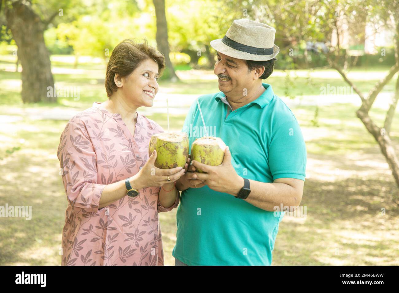 Happy indian senior couple having coconut water at summer park. Old people enjoying retirement life. Stock Photo