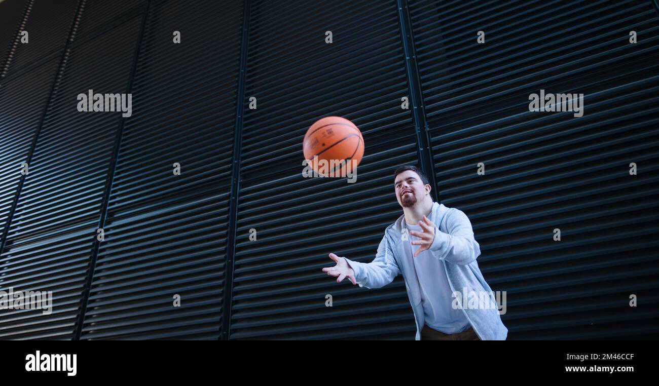 Young man with down syndrom throwing away basketball ball. Stock Photo