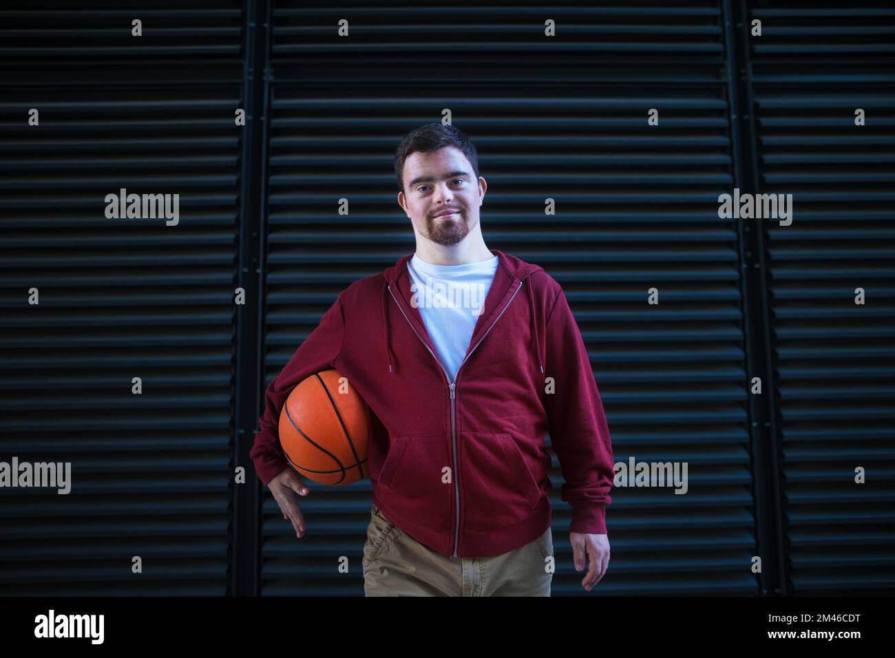 Portrait of young man with down syndrom holding basketball ball. Stock Photo
