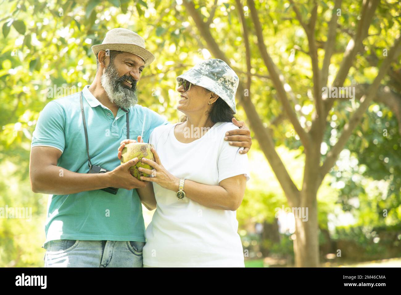 Happy indian mature couple having coconut water at summer park. senior people enjoying retirement life. Stock Photo